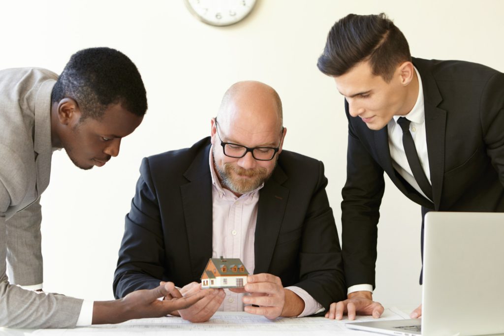 three-office-men-estimating-mock-up-model-future-terraced-house-caucasian-engineer-glasses-holding-miniature-smiling-other-colleagues-suits-looking-tiny-house-with-interest-home-loan-mortgage-broker